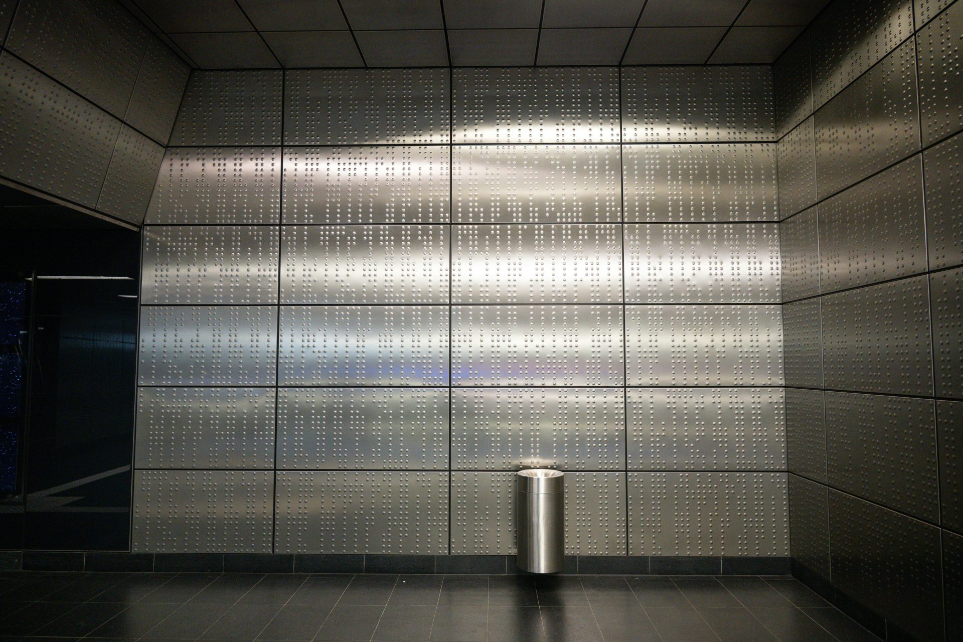 A metallic trash can against a tiled wall